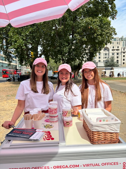 Three Orega team members in pink caps serving Mister Twist ice cream from an Orega cart at Finsbury Square Garden, Moorgate